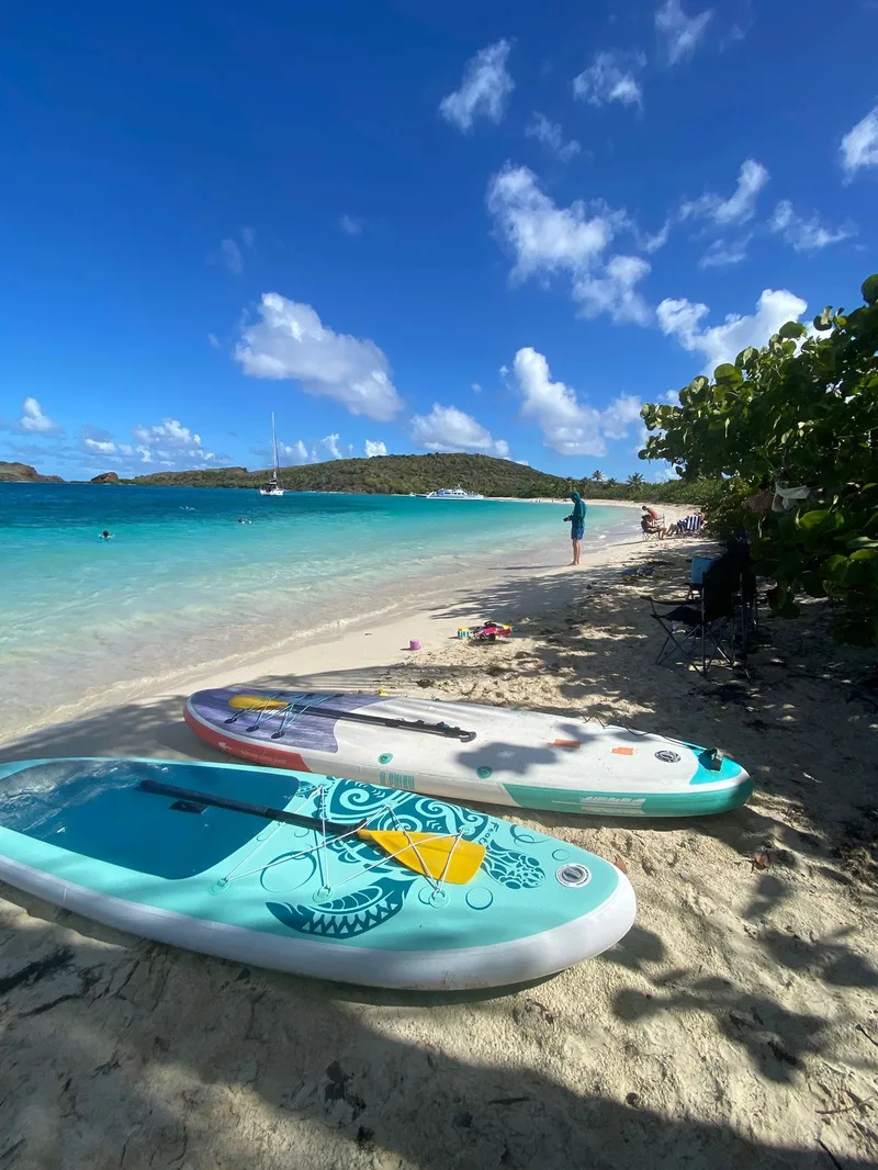 Quiet Culebrita beach with paddleboards on the sand and sailboats offshore
